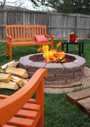 A charming fire pit, surrounded by brightly colored orange chairs and benches.